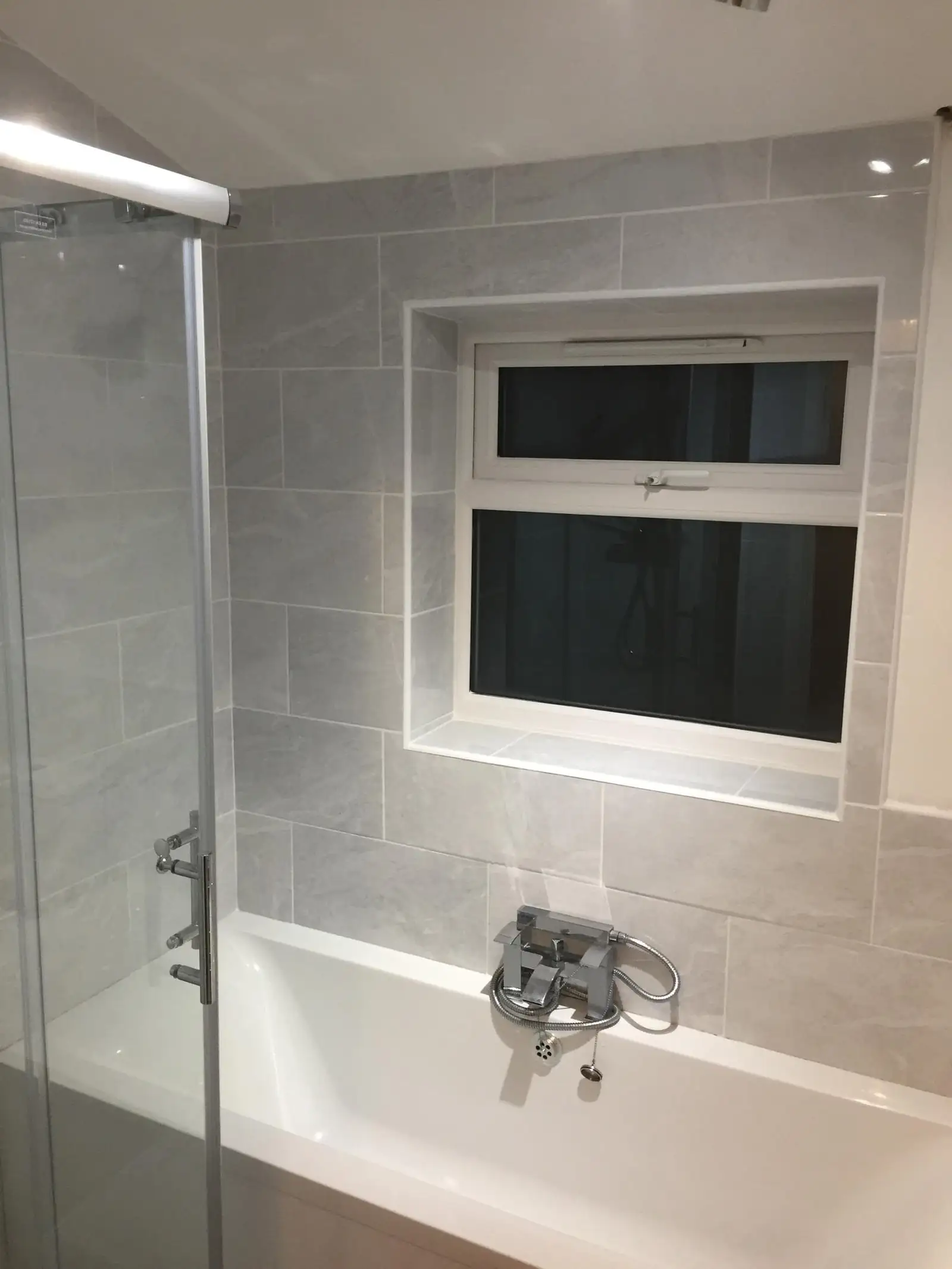 Bath with shower screen and grey wall tiles