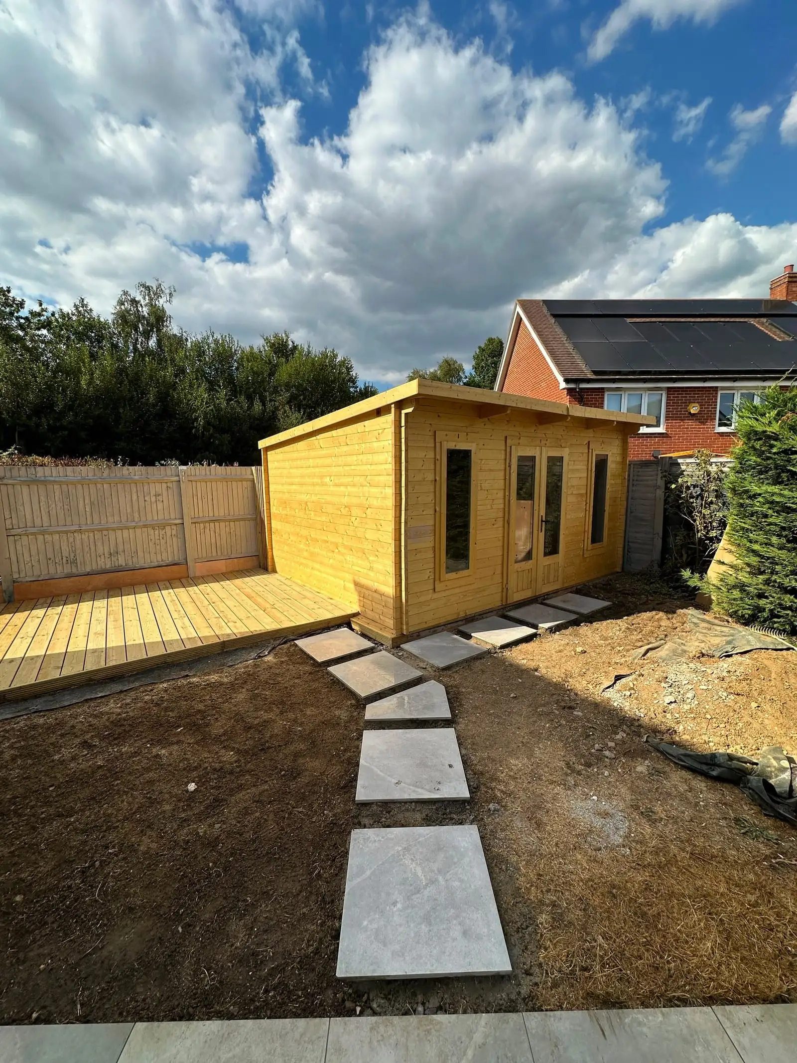 Timber garden room with glazed front, decking and stepping-stone path across the lawn