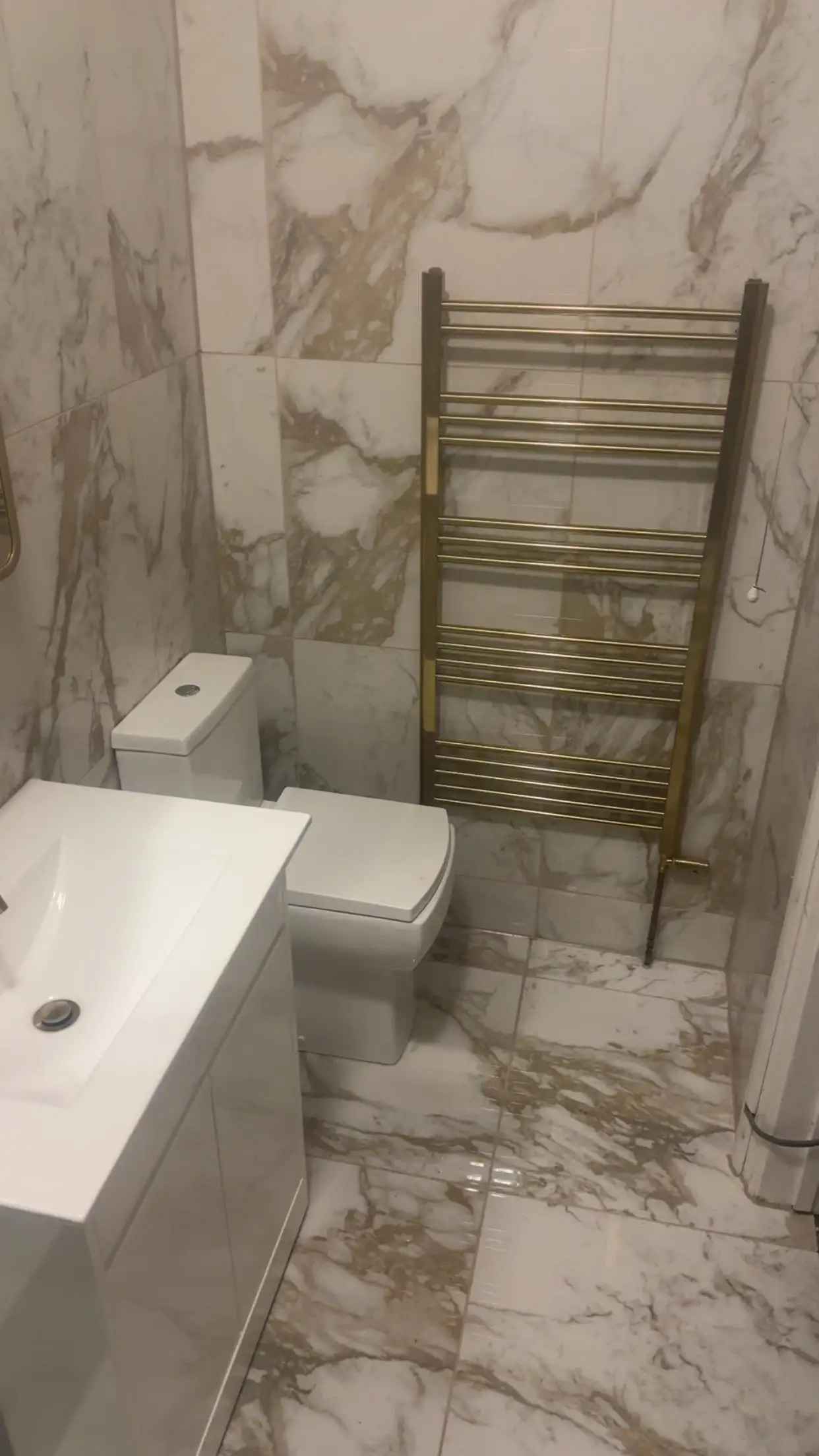 Renovated bathroom with marble-effect tiles, brushed gold towel radiator and white vanity
