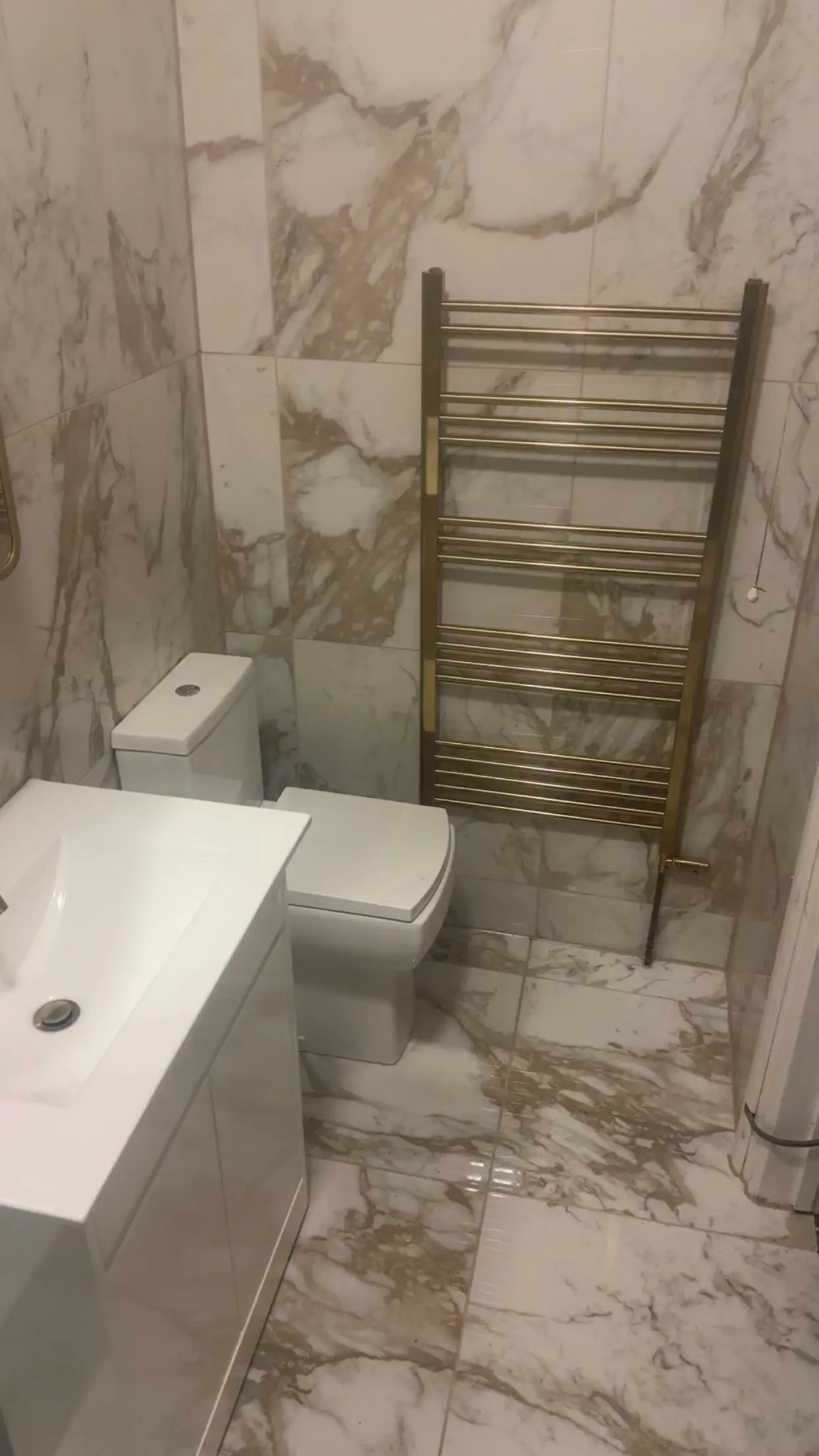 Bathroom with marble-effect wall and floor tiles, brushed gold towel radiator, white vanity and toilet
