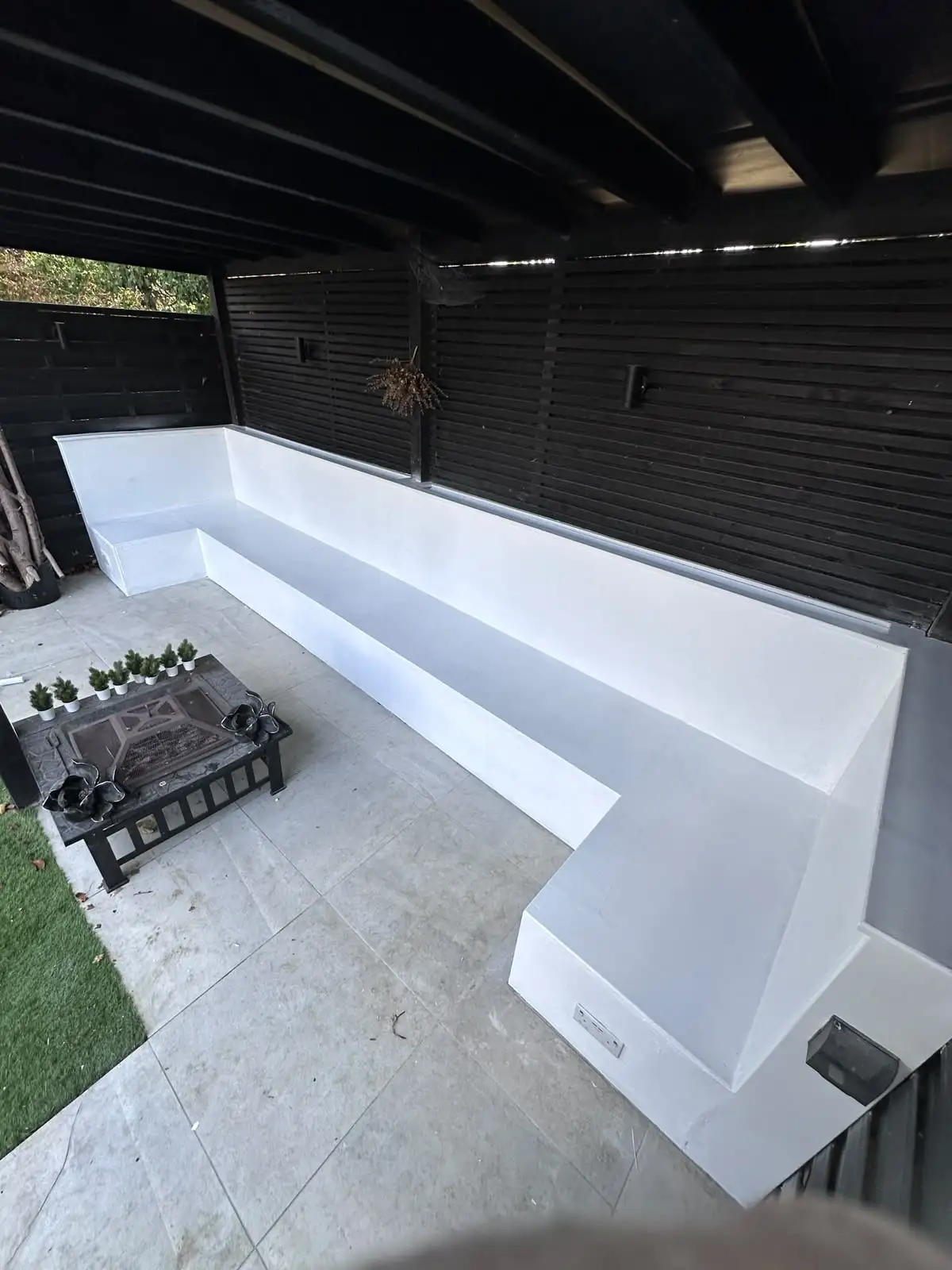 Porcelain patio with built-in white seating, fire pit and slatted pergola